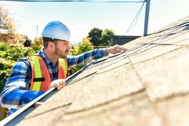 A homeowner reviewing roofing material samples with a contractor while standing in front of a residential home under a clear sky.