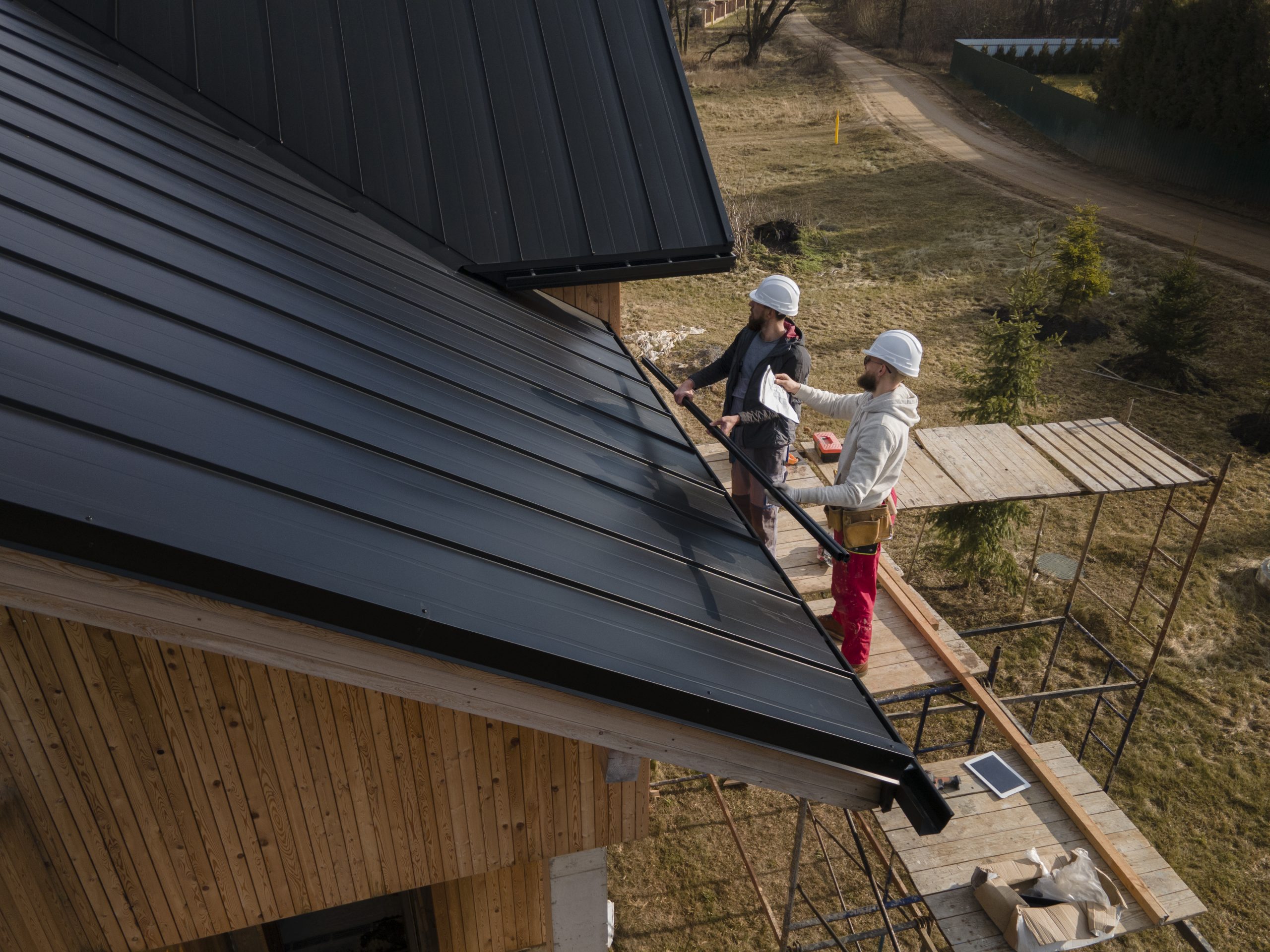 full-shot-roofers-working-with-helmets A spacious, well-maintained backyard deck attached to a home features outdoor dining furniture, cushioned seating, glass railings, and scenic landscaping, creating a safe and inviting space for outdoor living and entertaining.
